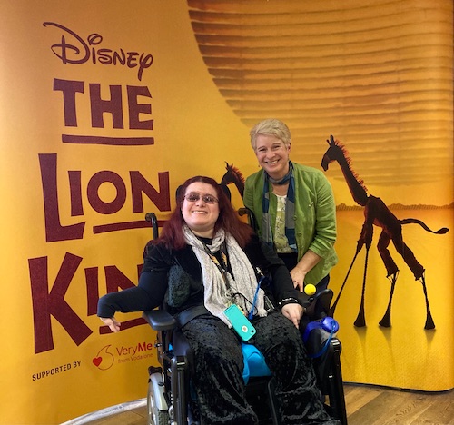 Emma and Carol stood next to The Lion King Musical poster