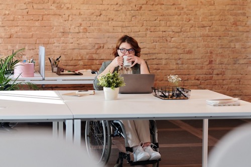 Woman sat at a desk, holding a drink and using a laptop